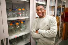 A student stands next to a cabinet full of bottles in a lab setting